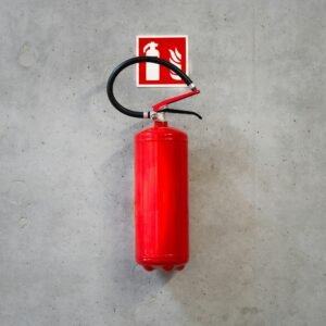 A red fire extinguisher mounted on a concrete wall indoors with emergency signage.
